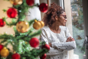 Woman standing by decorated tree staring out window